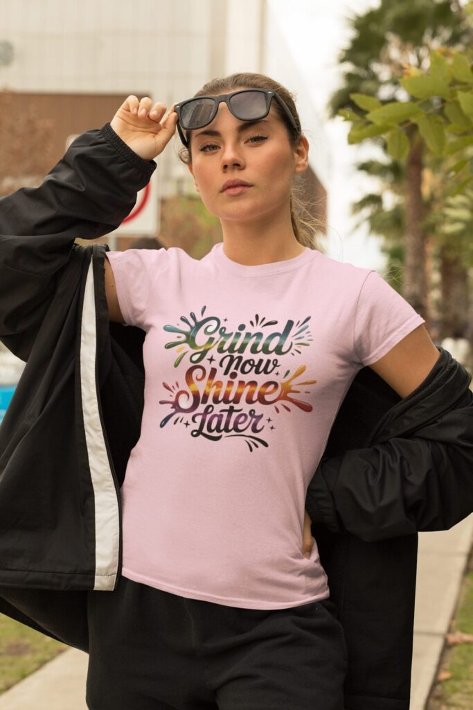 How Motivational T-Shirts Inspire Confidence Daily (+ Outfit Ideas) | Empowering T-Shirts by Quotnair Confident young woman wearing a pink motivational t-shirts with the colorful quote "Grind Now, Shine Later," styled with a black jacket and sunglasses in an urban outdoor setting.